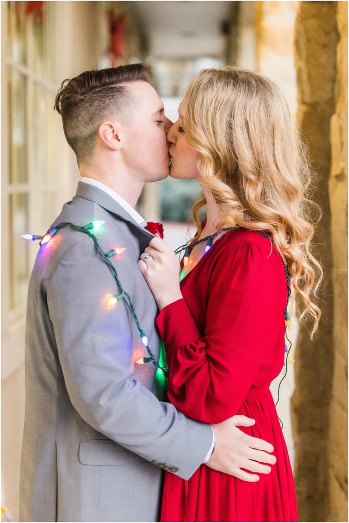 couple wrapped up in Christmas lights for their adriatica village engagement photos